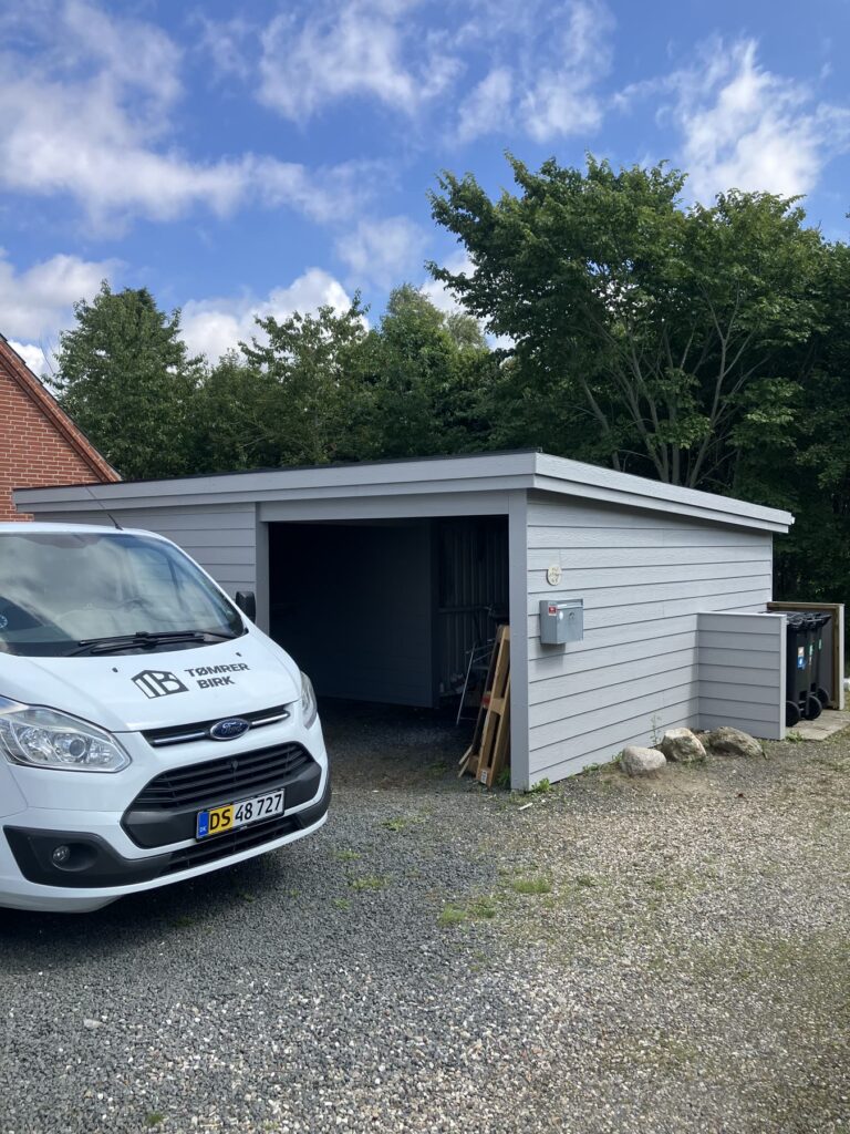 Grå carport med skur og Tømrer Birks varebil foran