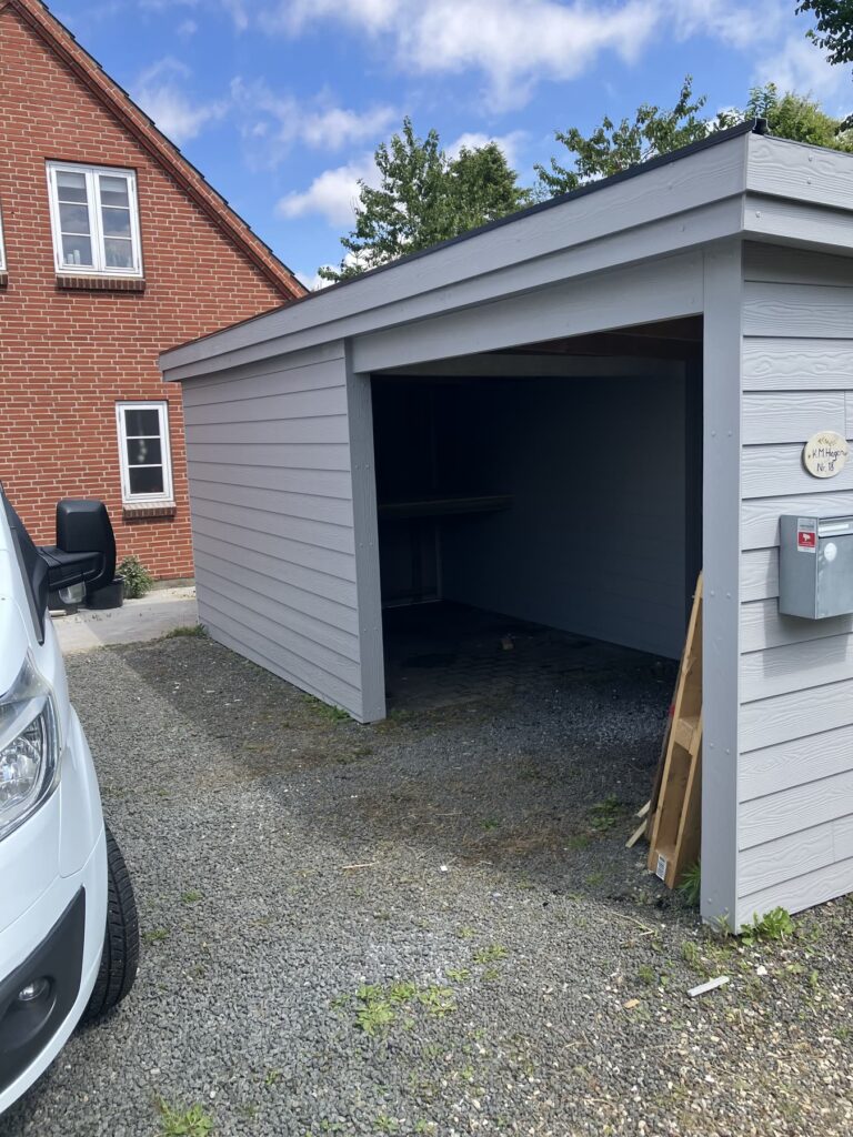 Åben grå carport med skur i enden