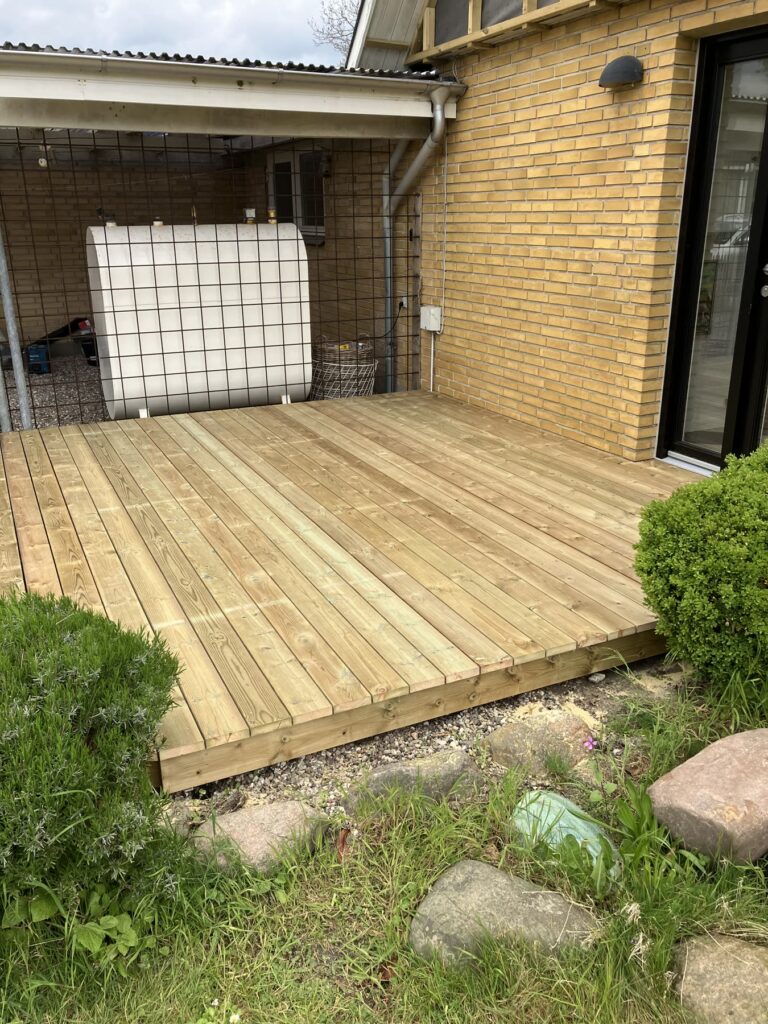 Træterrasse langs muren ved en gul murstensvilla
