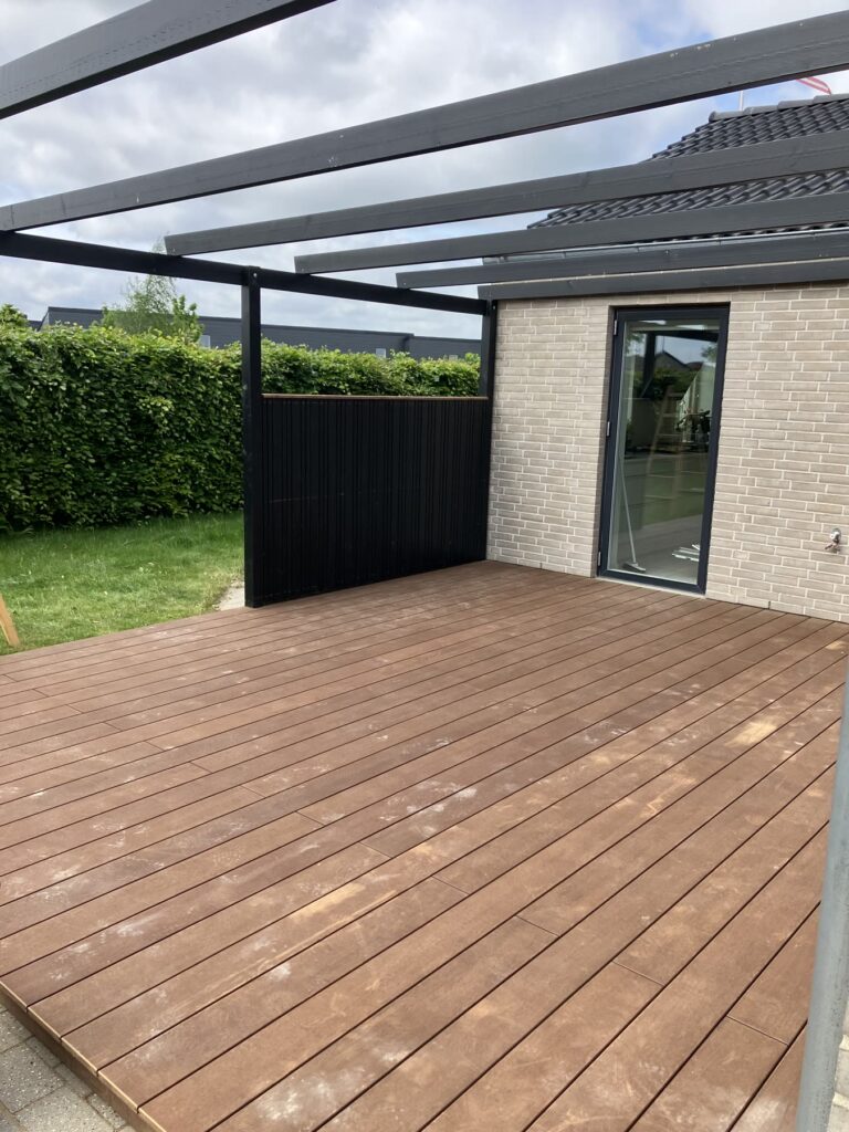 Kompositterrasse med sort pergola set fra haven