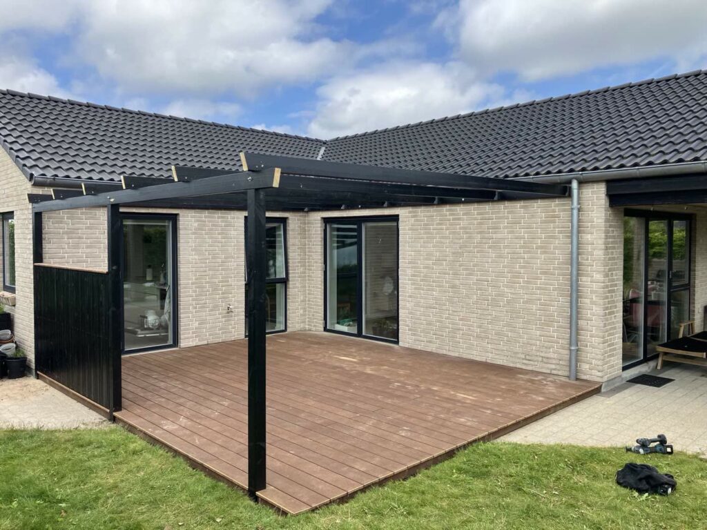 Kompositterrasse med sort pergola ved et parcelhus