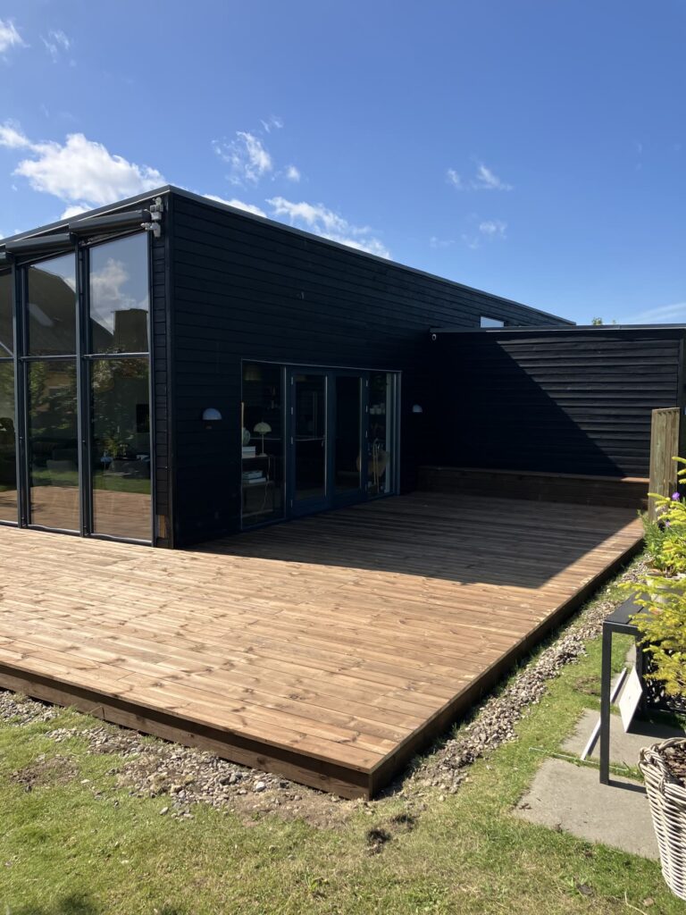 Ny træterrasse langs et sort hus set på skrå