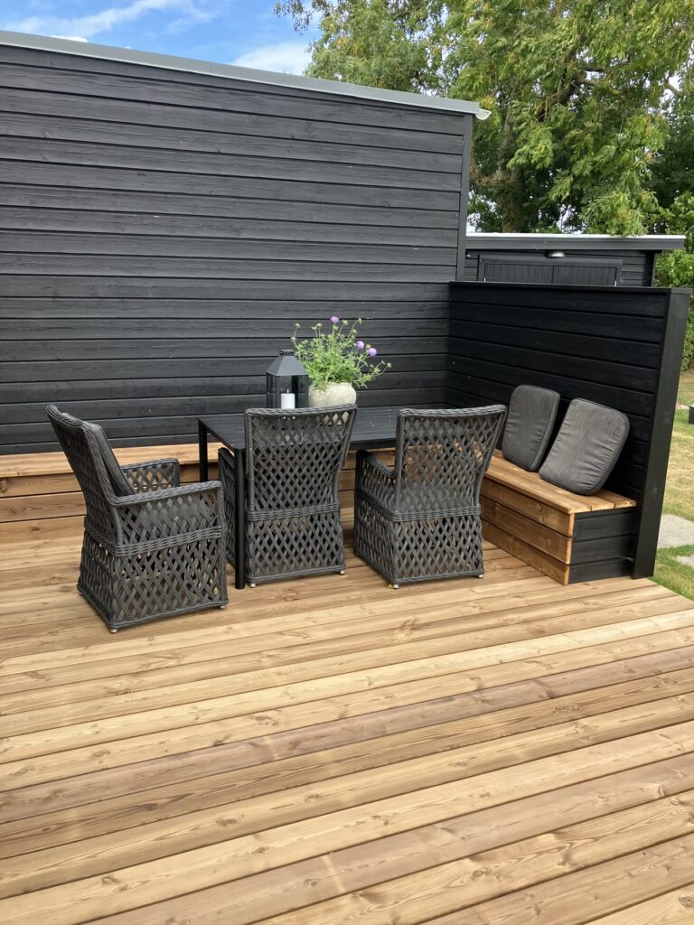 Hjørne af en træterrasse med loungemøbler og læhegn