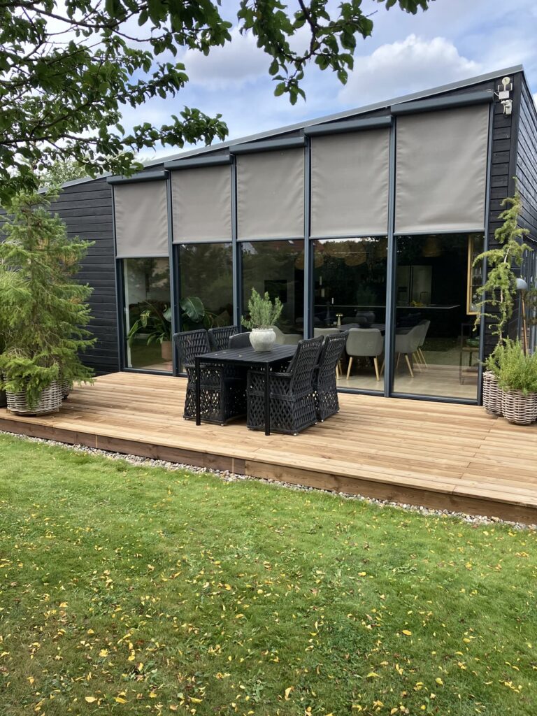 Træterrasse med spisebord foran store vinduespartier